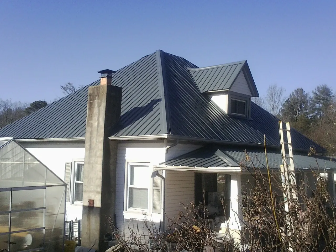 Dark blue standing seam metal roof on a white farmhouse with dormer — Slate & Tile Roof Repair by Roofing Brothers in Oakfield
