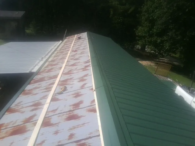 Old rusted panels beside newly installed green metal roofing — Wind Damage Roof Repair by Roofing Brothers in Oakfield