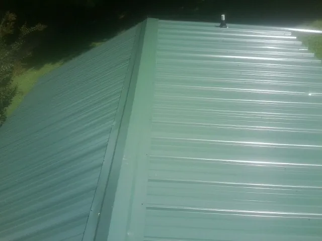 New green metal panels meeting at the ridge of a roof — Flat Roof Repair work by our crew in Oakfield